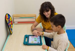 niño con autismo no verbal en terapia de logopedia usando tablet de comunicación alternativa (SAAC)